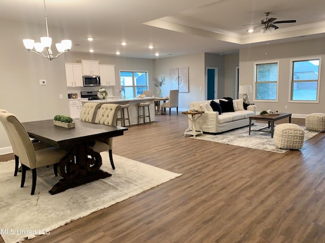 dining area featuring hardwood / wood-style floors, ceiling fan with notable chandelier, ornamental molding, and a raised ceiling