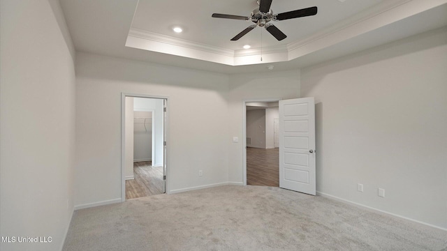 spare room featuring ceiling fan, light colored carpet, ornamental molding, and a raised ceiling