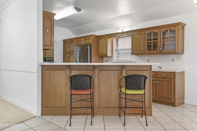 kitchen featuring light tile patterned flooring, lofted ceiling, a kitchen bar, stainless steel fridge, and backsplash