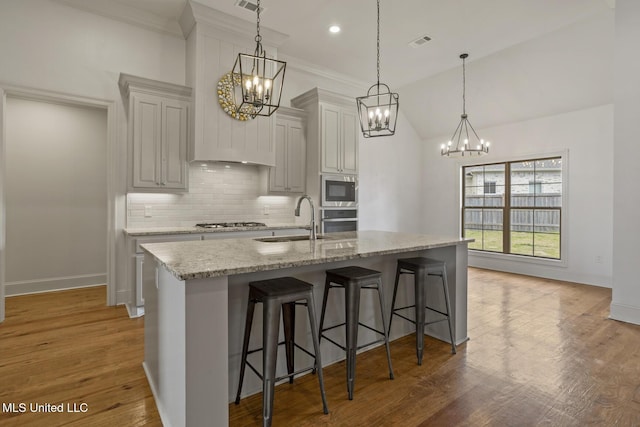 kitchen with stainless steel appliances, a breakfast bar, a sink, light wood-type flooring, and backsplash