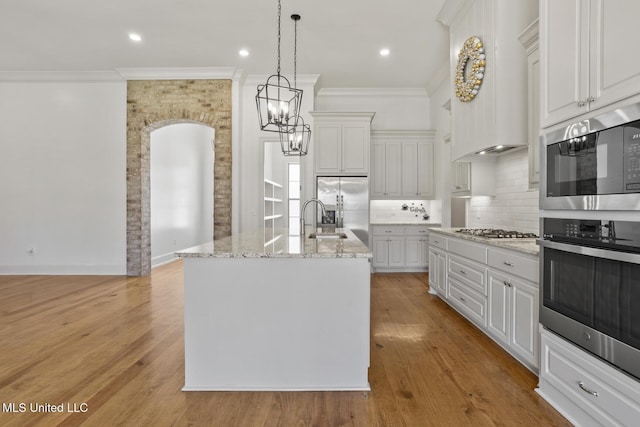 kitchen with appliances with stainless steel finishes, light wood-type flooring, light stone counters, and tasteful backsplash