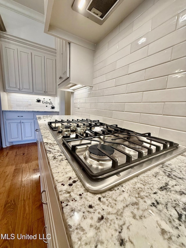 interior details with tasteful backsplash, light stone countertops, stainless steel gas stovetop, and wood finished floors