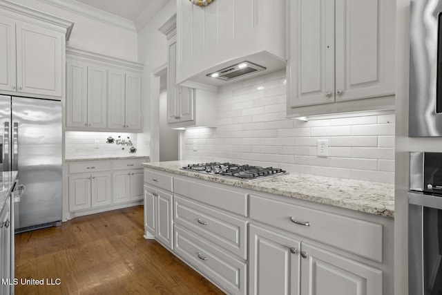 kitchen with dark wood-style floors, stainless steel appliances, crown molding, premium range hood, and white cabinetry