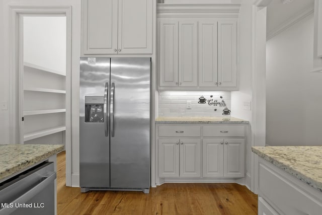 kitchen with light stone counters, stainless steel appliances, light wood-style floors, white cabinets, and backsplash