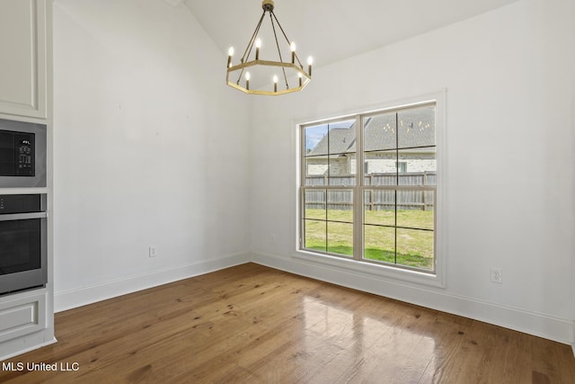 unfurnished dining area featuring a chandelier, lofted ceiling, wood-type flooring, and baseboards