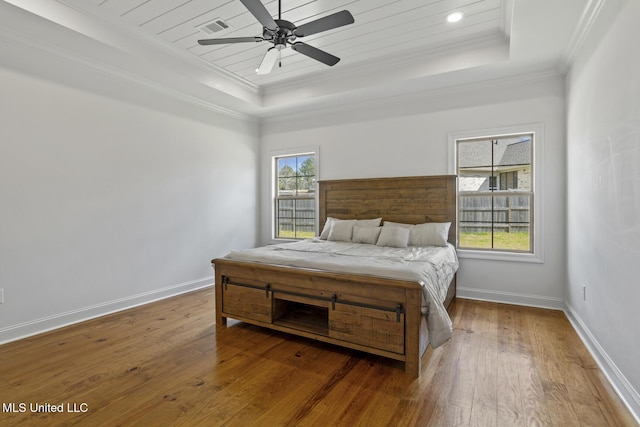 bedroom featuring a tray ceiling, visible vents, hardwood / wood-style floors, ornamental molding, and baseboards