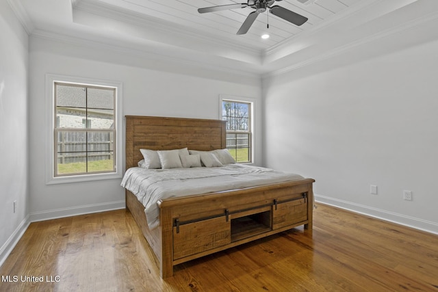 bedroom with a raised ceiling, baseboards, crown molding, and hardwood / wood-style floors