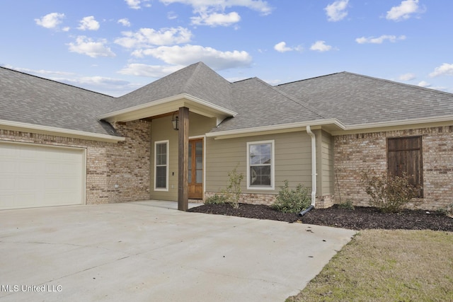 view of front of house featuring a garage, concrete driveway, brick siding, and roof with shingles