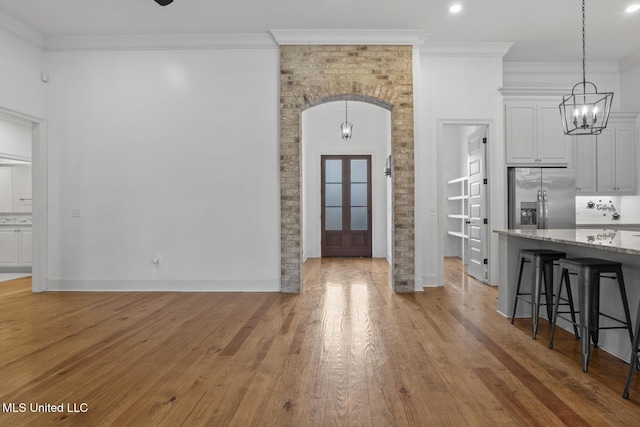 unfurnished dining area with baseboards, arched walkways, light wood-style flooring, crown molding, and a notable chandelier