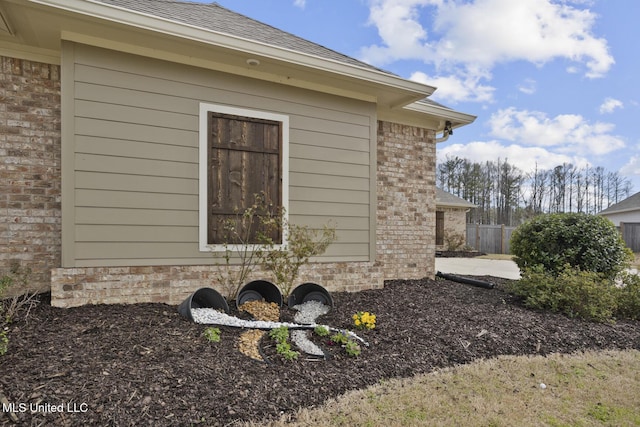 view of home's exterior featuring brick siding, fence, and roof with shingles