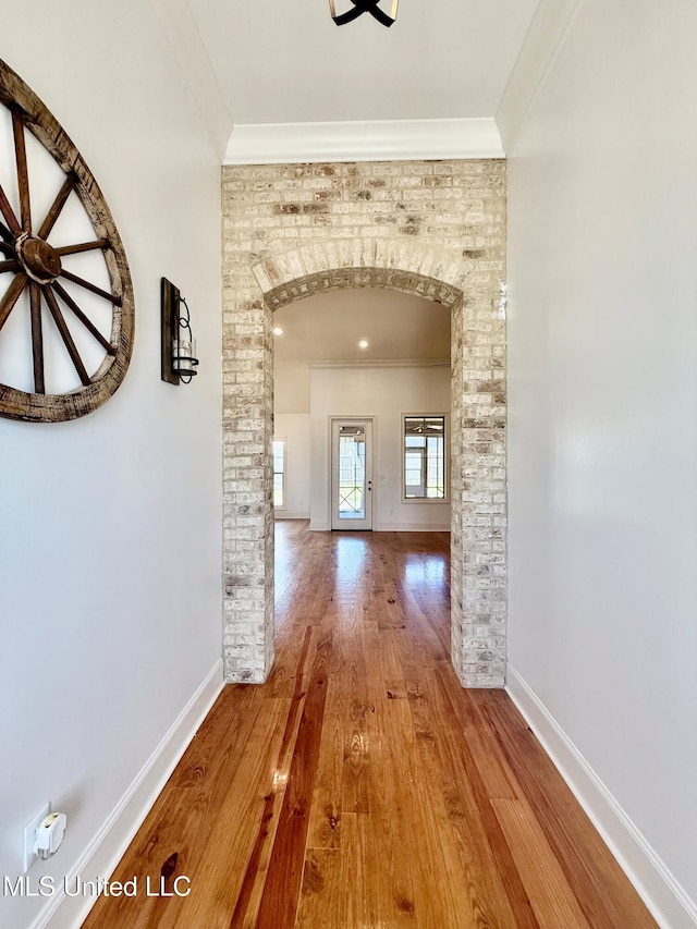 corridor featuring arched walkways, baseboards, wood finished floors, and crown molding