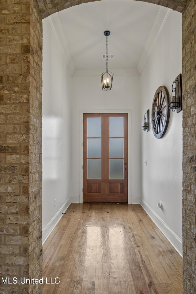 interior space with wood-type flooring, ornamental molding, a chandelier, and baseboards