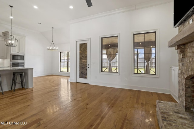 unfurnished living room with a fireplace with raised hearth, lofted ceiling, baseboards, ornamental molding, and light wood finished floors