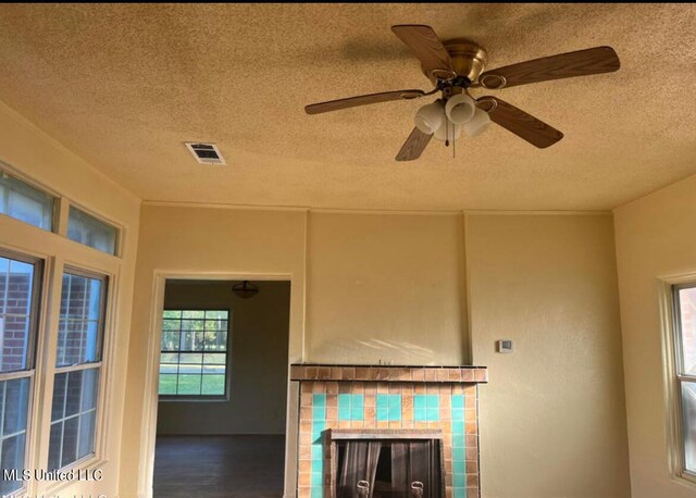 unfurnished living room with visible vents, wood finished floors, a textured ceiling, a tile fireplace, and a ceiling fan