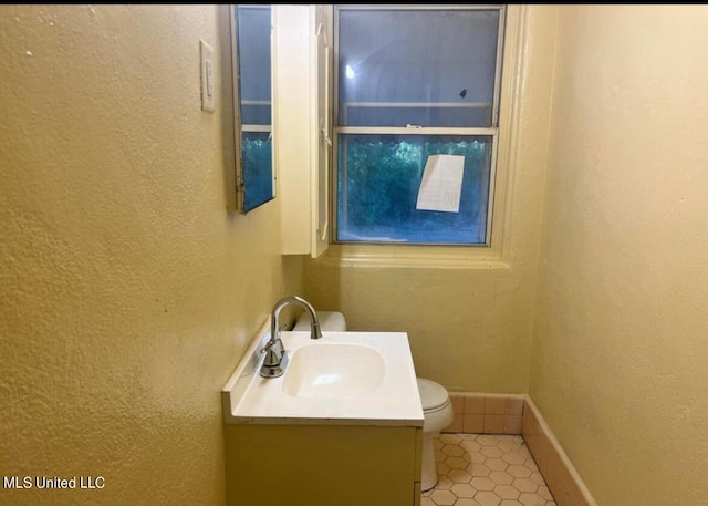 bathroom featuring vanity, baseboards, tile patterned floors, toilet, and a textured wall