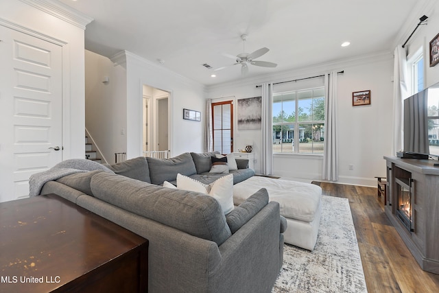 living room featuring dark wood-type flooring, ceiling fan, crown molding, and a fireplace