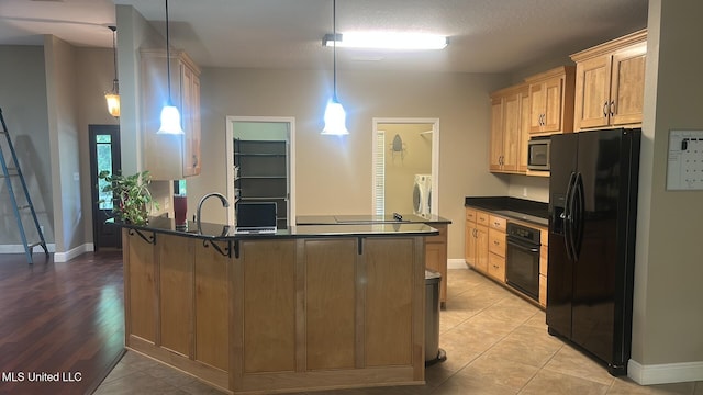 4509 Hickory St, Pascagoula, MS 39567 - kitchen featuring black appliances, a peninsula, dark countertops, washer / dryer, and light tile patterned floors