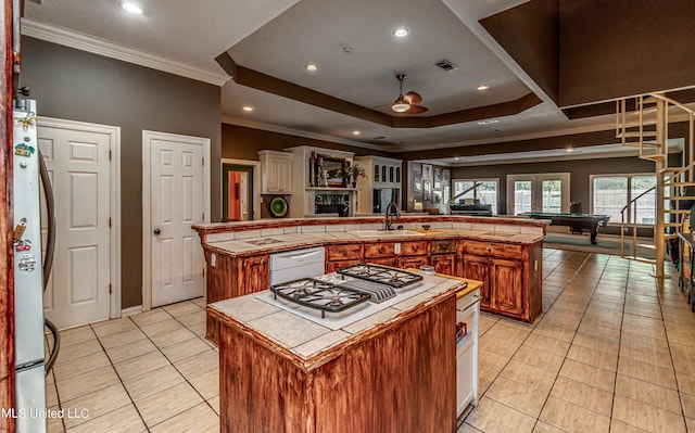 kitchen featuring crown molding, tile counters, light tile patterned flooring, a large island with sink, and white appliances