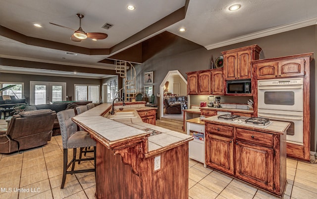 kitchen with a sink, a large island, a ceiling fan, white appliances, and tile counters