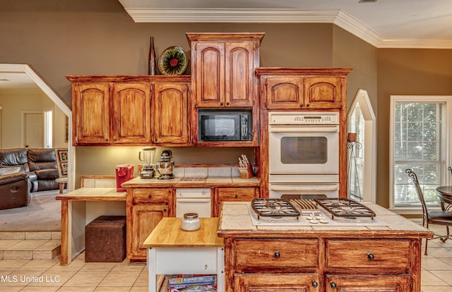 kitchen featuring a kitchen island, tile countertops, black microwave, ornamental molding, and light tile patterned floors