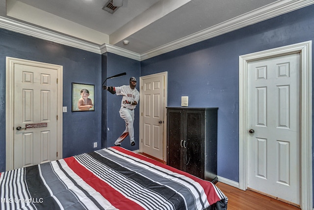 bedroom with wood finished floors, visible vents, baseboards, and ornamental molding