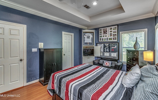 bedroom featuring a raised ceiling, visible vents, ornamental molding, light wood-style floors, and baseboards