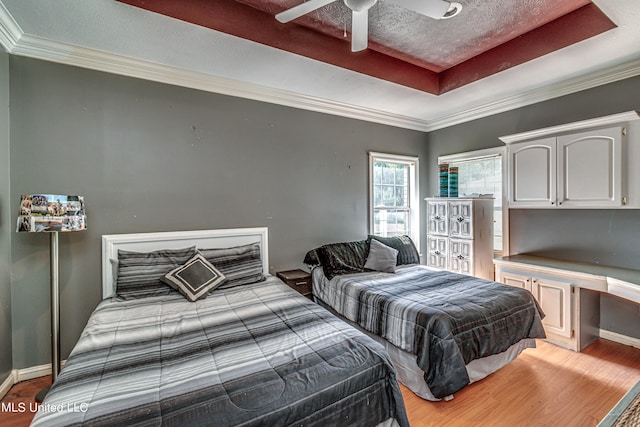 bedroom featuring ceiling fan, crown molding, a tray ceiling, and light wood-type flooring