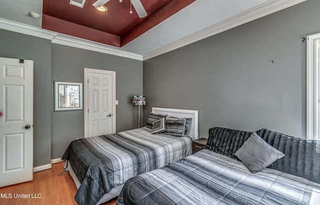 bedroom featuring a raised ceiling, wood finished floors, visible vents, ornamental molding, and baseboards