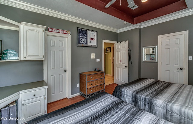 bedroom featuring a ceiling fan, wood finished floors, a raised ceiling, and crown molding