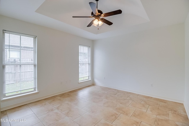 tiled empty room featuring ceiling fan and a tray ceiling