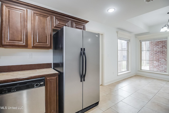 kitchen with dark brown cabinetry, stainless steel appliances, tile countertops, decorative light fixtures, and light tile patterned floors