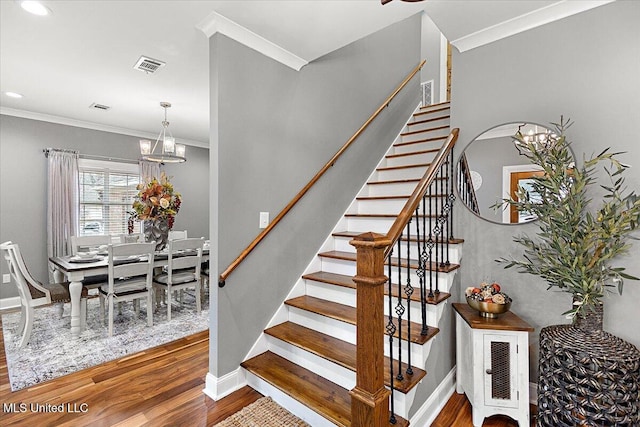 staircase with wood-type flooring, ornamental molding, and a notable chandelier