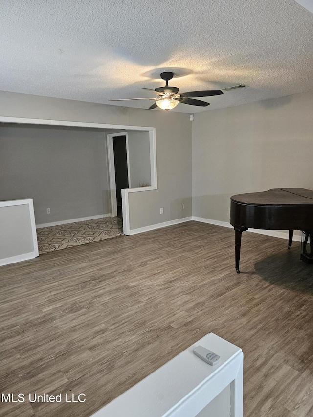 interior space featuring a ceiling fan, a textured ceiling, baseboards, and wood finished floors