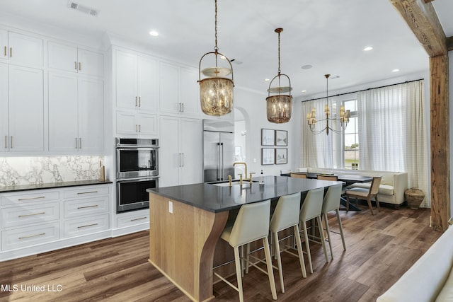 kitchen featuring appliances with stainless steel finishes, dark countertops, white cabinets, and an island with sink