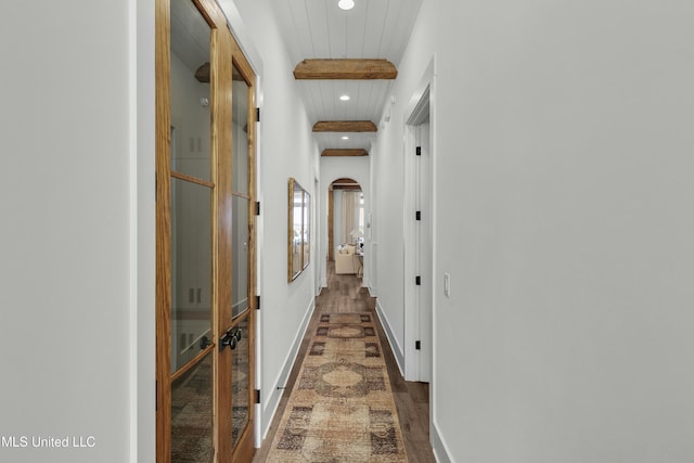 hallway featuring arched walkways, recessed lighting, baseboards, beamed ceiling, and dark wood finished floors