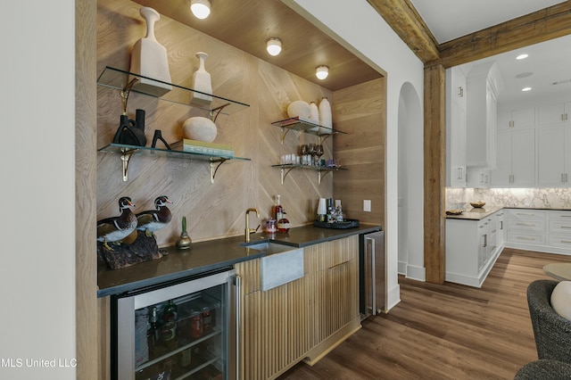 bar with beverage cooler, decorative backsplash, dark wood-type flooring, wet bar, and a sink