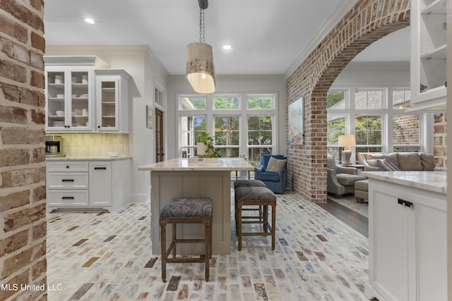 6416 Oliwa Pl, Diamondhead, MS 39525 - kitchen featuring ornamental molding, brick floors, open floor plan, white cabinetry, and light stone counters