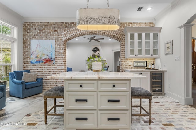 6416 Oliwa Pl, Diamondhead, MS 39525 - kitchen featuring wine cooler, a breakfast bar area, a ceiling fan, light stone counters, and ornamental molding