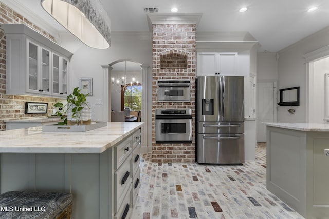 6416 Oliwa Pl, Diamondhead, MS 39525 - kitchen with stainless steel appliances, brick floors, light stone countertops, glass insert cabinets, and crown molding