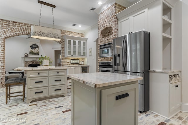 6416 Oliwa Pl, Diamondhead, MS 39525 - kitchen with stainless steel appliances, a kitchen island, ornamental molding, a fireplace, and glass insert cabinets