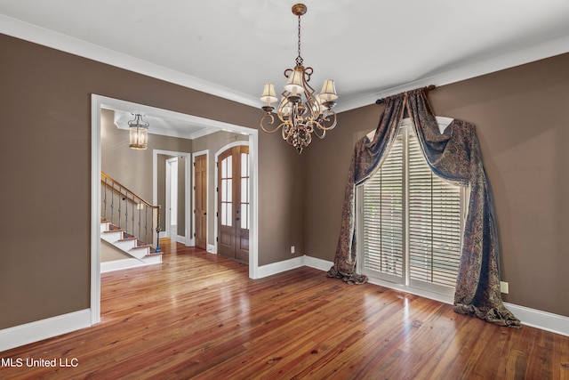 empty room with an inviting chandelier, french doors, ornamental molding, and hardwood / wood-style flooring