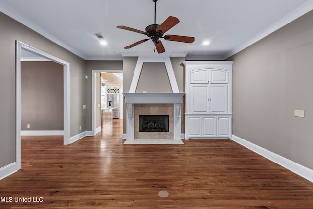 unfurnished living room with ornamental molding, a tiled fireplace, dark wood-type flooring, and ceiling fan