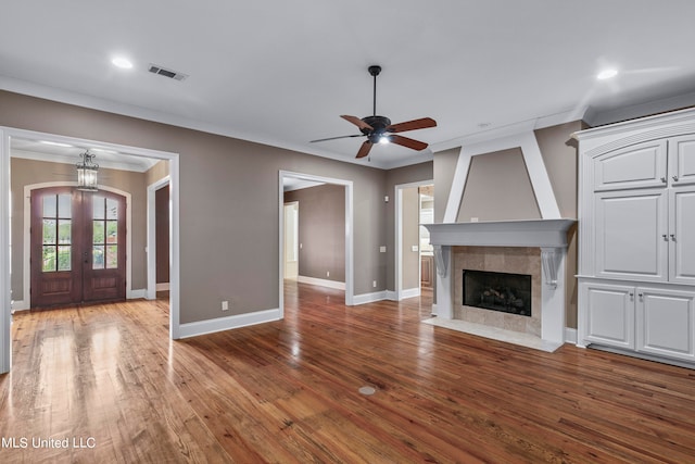 unfurnished living room featuring french doors, wood-type flooring, a large fireplace, ornamental molding, and ceiling fan