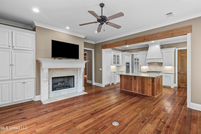 kitchen with a kitchen island, white cabinetry, a tiled fireplace, custom range hood, and dark wood-type flooring