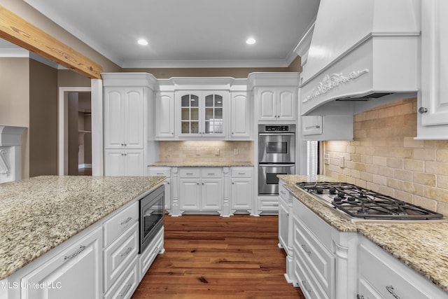 kitchen with custom exhaust hood, backsplash, appliances with stainless steel finishes, white cabinetry, and dark wood-type flooring