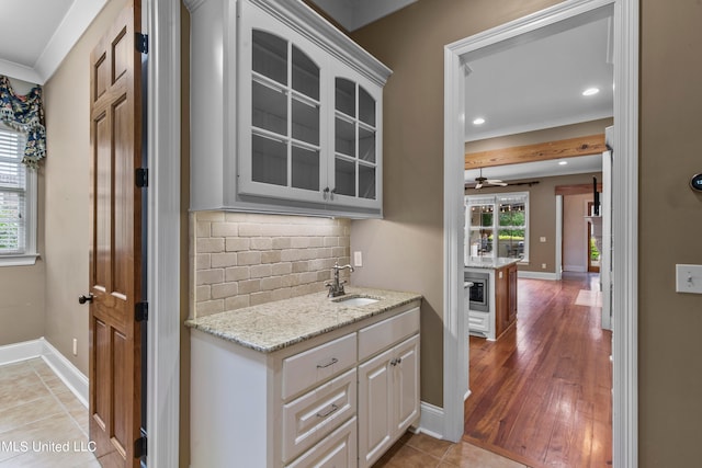 kitchen with backsplash, white cabinetry, light stone countertops, light hardwood / wood-style floors, and sink