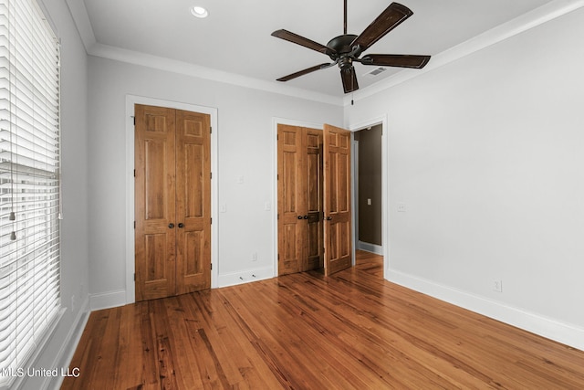 unfurnished bedroom with ornamental molding, hardwood / wood-style floors, multiple closets, and ceiling fan