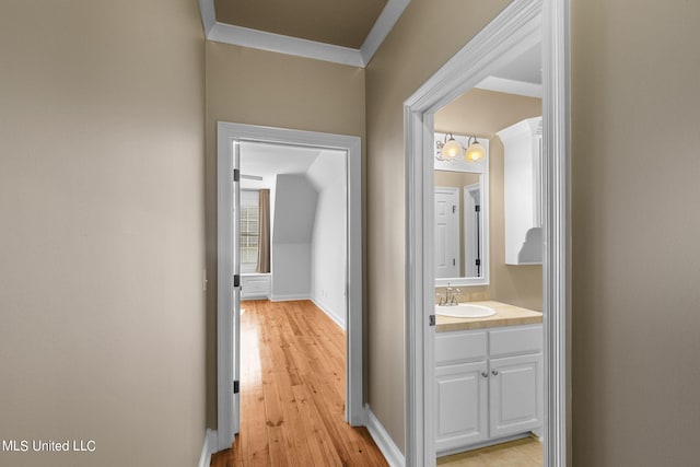 corridor with light hardwood / wood-style floors, crown molding, and sink