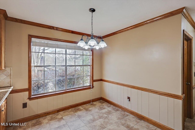 unfurnished dining area with a chandelier, ornamental molding, and wainscoting