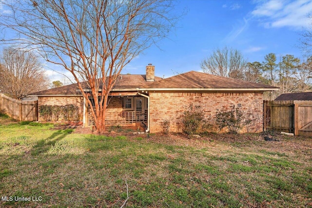 rear view of property featuring a yard, brick siding, a chimney, and fence